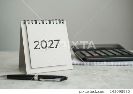 2027 desk calendar with pen, calculator and notepad on desktop. Financial planning, budgeting, corporate goals, tax planning concept 2027 desk calendar with pen, calculator and notepad on desktop. Financial planning, budgeting, corporate goals, tax planning concept 143098980