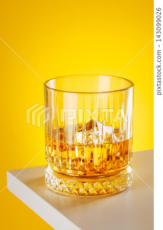 Whiskey glass with ice on yellow background minimal drink still life 143099026