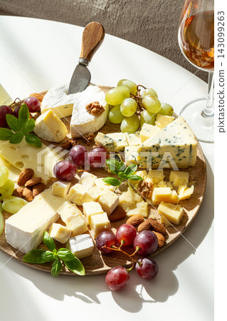 Assortment of gourmet cheeses with grapes nuts and a glass of rose wine Assortment of gourmet cheeses with grapes nuts and a glass of rose wine 143099263