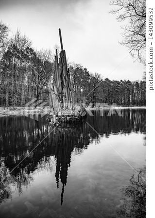 Basalt organ rises above the water at Rakotz lake in Germany. Nearby trees reflect on the water surface. The scene shows a stark landscape in monochrome. Basalt organ rises above the water at Rakotz lake in Germany. Nearby trees reflect on the water surface. The scene shows a stark landscape in monochrome. 143099532