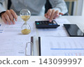 Business accountant reviewing financial charts and data performance in office with hourglass on desk. Time management and financial analysis concept. 143099997