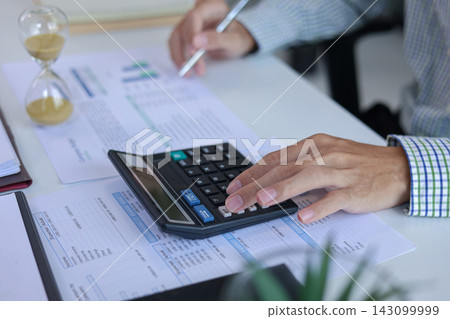 Businessman Calculating Financial Budget with Hourglass Clock on Desk. Time Management Concept. Businessman Calculating Financial Budget with Hourglass Clock on Desk. Time Management Concept. 143099999