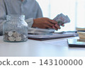 Close up glass jars filled with money and coins with businessman counting money in background. 143100000