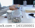 Close up glass jars filled with money and coins with businessman counting money in background. 143100001