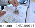 Businessman carefully stacking silver coins on top of documents that feature various business charts and data visualizations. financial planning or investment tracking concept. 143100014