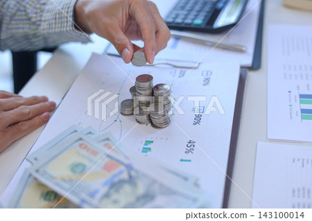 Businessman carefully stacking silver coins on top of documents that feature various business charts and data visualizations. financial planning or investment tracking concept. 143100014