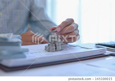 Businessman carefully stacking silver coins on top of documents that feature various business charts and data visualizations. financial planning or investment tracking concept. 143100015