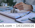 Businessman placing coin on top of coinstacks while engaging in financial planning or investment tracking on office desk 143100016