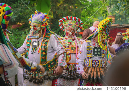 Traditional Bulgarian Kukeri, colorful festival costumes. Group of masked performers in authentic elaborate beaded masks, embroidered costumes, folklore celebration in forest. Cultural heritage scene Traditional Bulgarian Kukeri, colorful festival costumes. Group of masked performers in authentic elaborate beaded masks, embroidered costumes, folklore celebration in forest. Cultural heritage scene 143100596