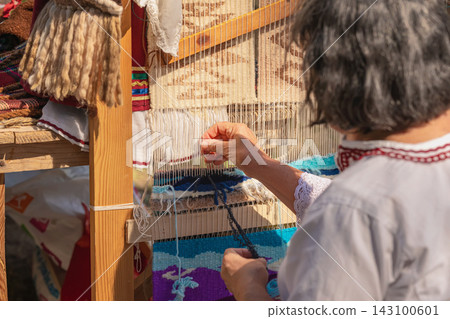 Woman Weaving Traditional Carpet on Wooden Loom in Kotel, Bulgaria. Woman demonstrates traditional carpet weaving on wooden loom during cultural festival dedicated to local crafts, textile heritage 143100601