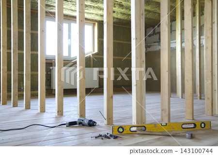 Close-up of professional tools: electrical screwdriver, level and measuring tape on background of wooden frame for future wall in attic room under reconstruction. Renovation and improvement concept. Close-up of professional tools: electrical screwdriver, level and measuring tape on background of wooden frame for future wall in attic room under reconstruction. Renovation and improvement concept. 143100744