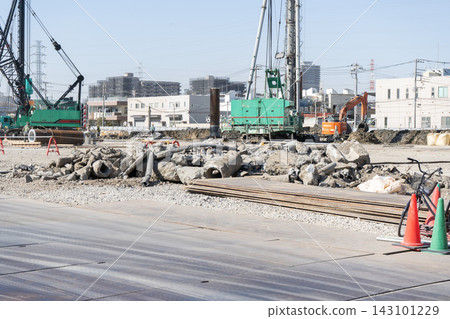Concrete rubble and steel plates piled up at the foundation construction site of a large building, with heavy machinery for pile driving lined up in the background. Concrete rubble and steel plates piled up at the foundation construction site of a large building, with heavy machinery for pile driving lined up in the background. 143101229