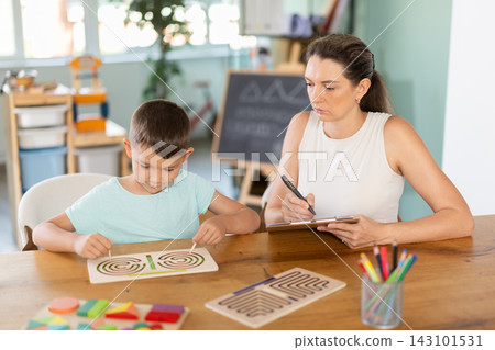 Child psychologist observing boy tracing labyrinths with both hands Child psychologist observing boy tracing labyrinths with both hands 143101531