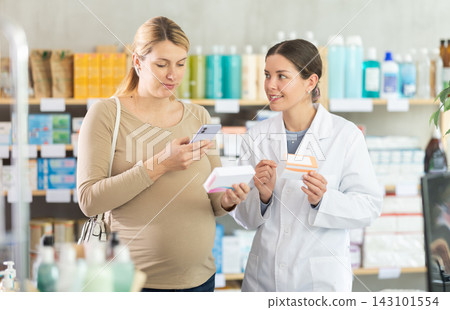 Pregnant woman in pharmacy scans QR code on vitamin pills product, pharmacist consulting client Pregnant woman in pharmacy scans QR code on vitamin pills product, pharmacist consulting client 143101554