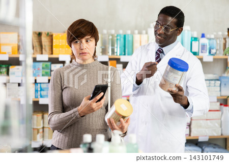 Woman in pharmacy scans QR code on infant formula. African man pharmacist in background Woman in pharmacy scans QR code on infant formula. African man pharmacist in background 143101749
