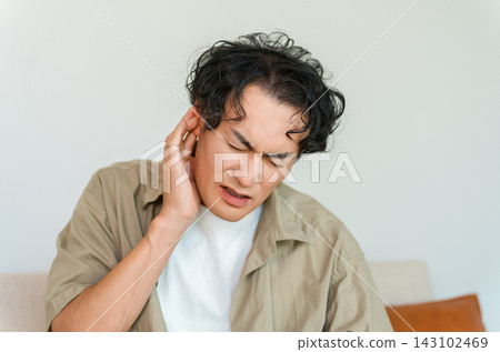 A man in his 40s, clutching his ear in pain. This image evokes images of ear problems such as tinnitus or otitis media. A man in his 40s, clutching his ear in pain. This image evokes images of ear problems such as tinnitus or otitis media. 143102469