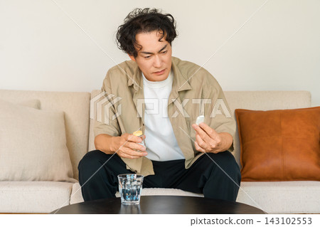 一位四十多歲的男子在家中測量體溫。這讓人聯想到因發燒或感冒而感到不適的畫面。 一位四十多歲的男子在家中測量體溫。這讓人聯想到因發燒或感冒而感到不適的畫面。 143102553
