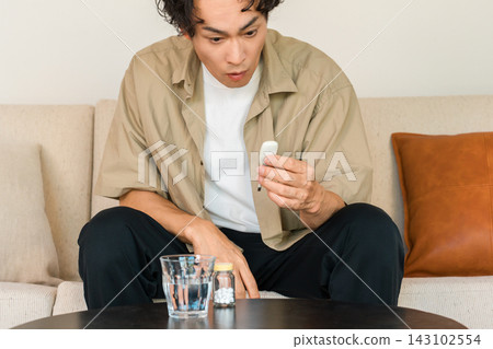 一位四十多歲的男子看到體溫計上的讀數時感到驚訝。這生動地展現了突發高燒或高燒是疾病徵兆的典型形象。 143102554