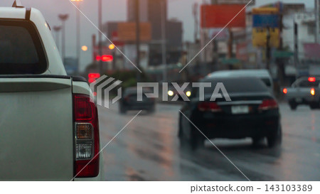 Close-up rear view of a white pickup car driving in urban traffic. Asphalt road wet from rain under dim daylight. Many cars are driving through the rain. Close-up rear view of a white pickup car driving in urban traffic. Asphalt road wet from rain under dim daylight. Many cars are driving through the rain. 143103389