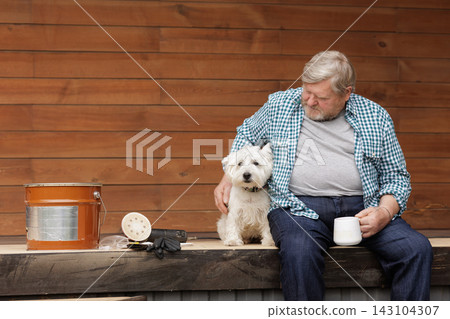 Terrace oil maintenance setup shows a homeowner, wooden deck, bucket, sanding tools, gloves, and dog during outdoor renovation. 143104307