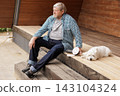 Senior homeowner sits beside a dog and orbital sander on a wooden terrace, illustrating outdoor maintenance, renovation, and do-it-yourself home improvement. 143104324