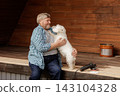 Senior man embraces his pet dog on a wooden home porch, illustrating companionship and relaxed aging for lifestyle and renovation campaigns. 143104328
