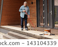 Senior man sweeps a wooden front porch beside a dog, illustrating active home maintenance, household care, and independent living for lifestyle campaigns. 143104339