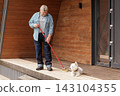 Senior homeowner sweeps a wooden front porch beside his dog, illustrating outdoor house maintenance, pet companionship, and independent daily living. 143104355