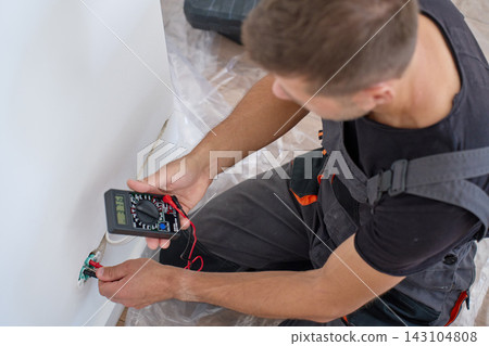 Man testing electrical wires in wall with digital multimeter Man testing electrical wires in wall with digital multimeter 143104808