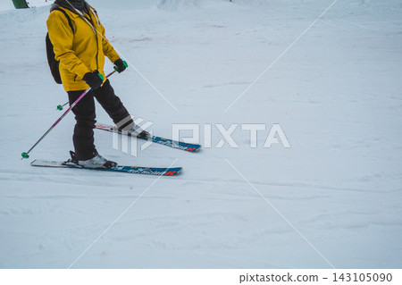 一名身穿黃色滑雪服的女子正在滑雪下山。 143105090