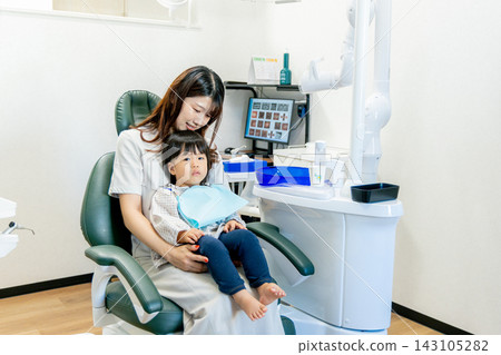 牙齒保健員在牙科診所的檢查椅上檢查一位母親和她 2 歲孩子的牙齒。 143105282