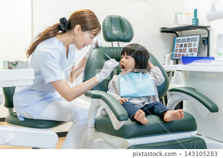 牙齒保健員在牙科診所的檢查椅上檢查一位母親和她 2 歲孩子的牙齒。 143105283