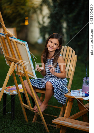 Happy elementary age girl painting outdoors with easel Happy elementary age girl painting outdoors with easel 143105429