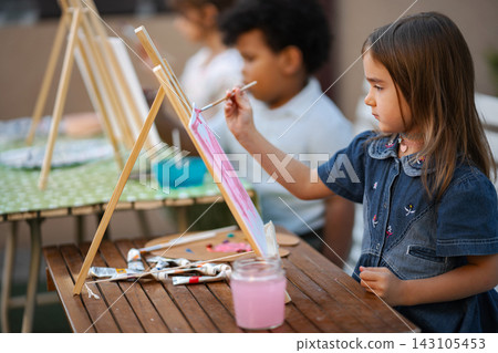 Young girl painting on easel during outdoor art class Young girl painting on easel during outdoor art class 143105453