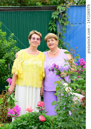 Authentic portrait of two smiling senior russian sisters 80 and 75 years old with flower bouquets standing in a summer garden in Russia Authentic portrait of two smiling senior russian sisters 80 and 75 years old with flower bouquets standing in a summer garden in Russia 143106976