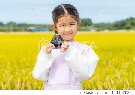 一個孩子手捧飯糰站在稻田前。 一個孩子手捧飯糰站在稻田前。 143107025
