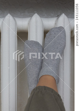 Legs of a person in gray socks keeping feet warm on a home heating radiator panel Legs of a person in gray socks keeping feet warm on a home heating radiator panel 143111056