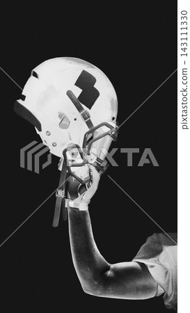 American football helmet raised in hand against black background in black white sport poster style American football helmet raised in hand against black background in black white sport poster style 143111330
