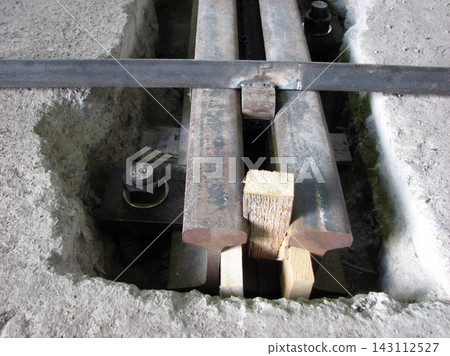 Close-up view of steel railway rails mounted in a concrete recess during track installation, featuring wooden spacer blocks, heavy anchor bolts, and a welded crossbar for alignment Close-up view of steel railway rails mounted in a concrete recess during track installation, featuring wooden spacer blocks, heavy anchor bolts, and a welded crossbar for alignment 143112527