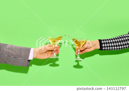 Two hands toasting martini cocktails on green background 143112797