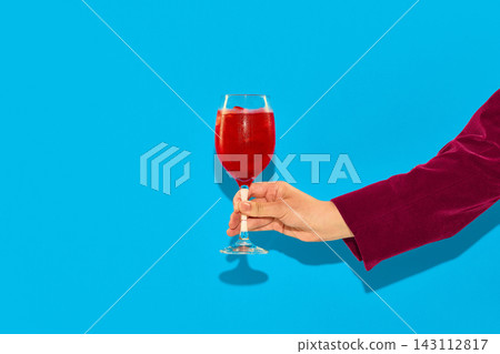 Hand holding red spritz cocktail on blue background. 143112817