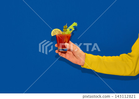 Hand holding bloody mary cocktail on blue background. Hand holding bloody mary cocktail on blue background. 143112821