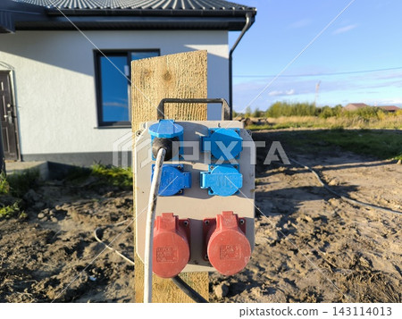 Power panel with sockets on a pole near a house under construction Power panel with sockets on a pole near a house under construction 143114013