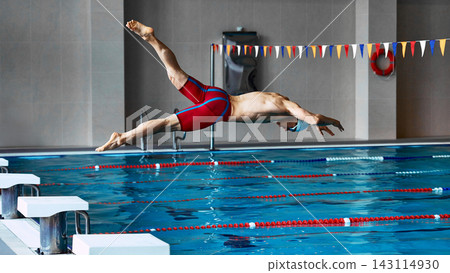 Competitive swimmer diving into indoor pool from starting block. Competitive swimmer diving into indoor pool from starting block. 143114930