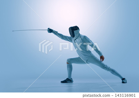 Male fencer performing powerful attacking lunge with epee in modern studio. Male fencer performing powerful attacking lunge with epee in modern studio. 143116901