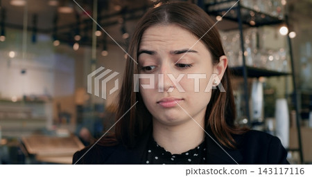 Brunette woman shows doubtful face during quiet moment. Contemplative young adult furrows brow thoughtfully, glancing downward with skeptical demeanor and visible uncertainty inside modern space. Brunette woman shows doubtful face during quiet moment. Contemplative young adult furrows brow thoughtfully, glancing downward with skeptical demeanor and visible uncertainty inside modern space. 143117116