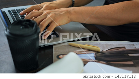 Hands typing on laptop beside coffee cup, notebook, and magazine on desk, showing focused work, writing, editing, remote office tasks, and everyday productivity in close workspace view Hands typing on laptop beside coffee cup, notebook, and magazine on desk, showing focused work, writing, editing, remote office tasks, and everyday productivity in close workspace view 143117118