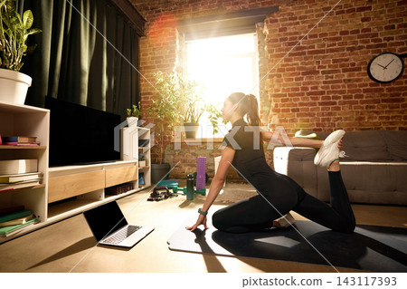 Woman stretching quadriceps on mat during online home workout. Woman stretching quadriceps on mat during online home workout. 143117393