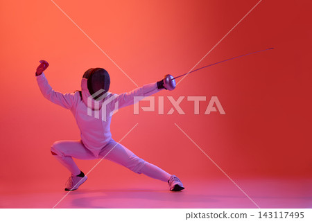 Female fencer holding powerful low guard position under vibrant red lighting. 143117495