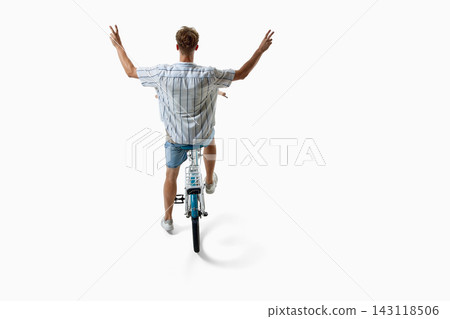 Carefree young man rides bicycle with arms raised from rear view Carefree young man rides bicycle with arms raised from rear view 143118506